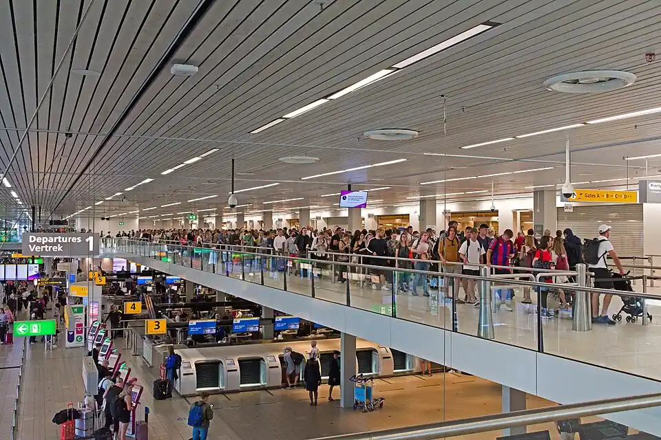 Travellers queuing for security in a large hall at Amsterdam Schiphol