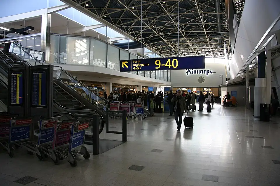 A terminal hall at Helsinki Airport with escalators, gate signs and luggage trolleys
