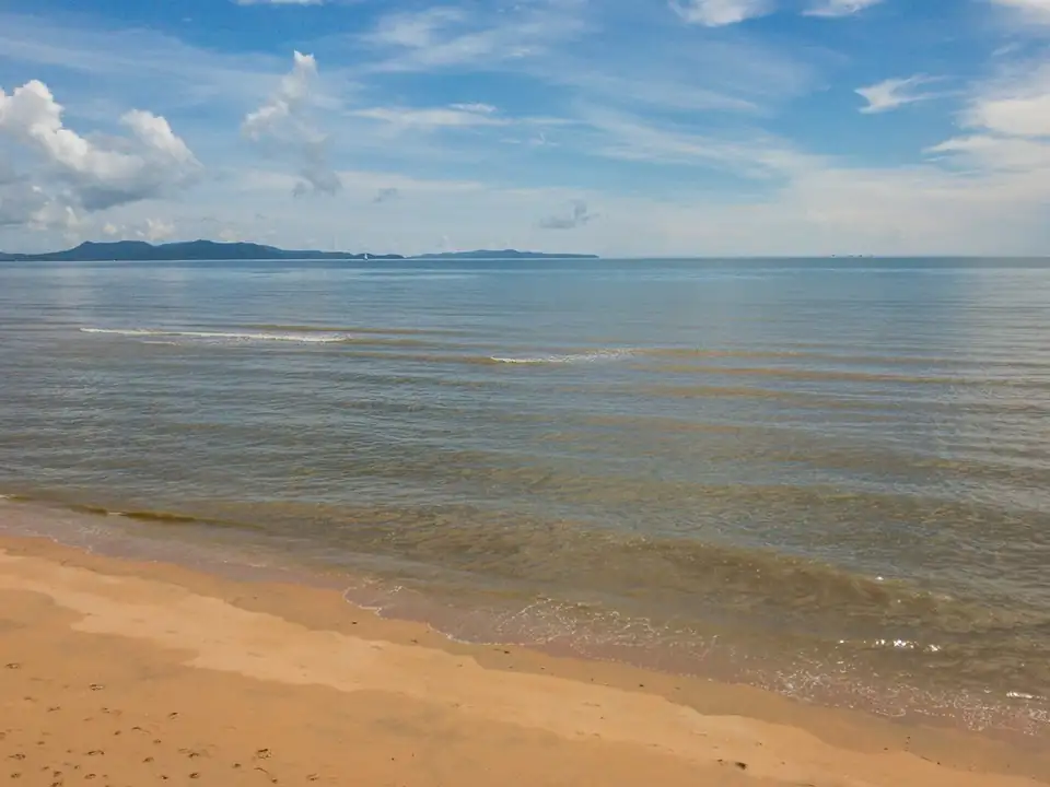 Calm water lapping onto the sand at Jomtien Beach, islands on the horizon