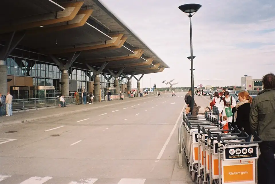 The kerb outside Oslo Gardermoen terminal under its long wooden roof, luggage trolleys lined up