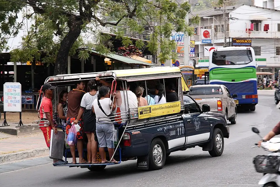 A dark blue songthaew pickup taxi on a Pattaya street, passengers standing on its back step