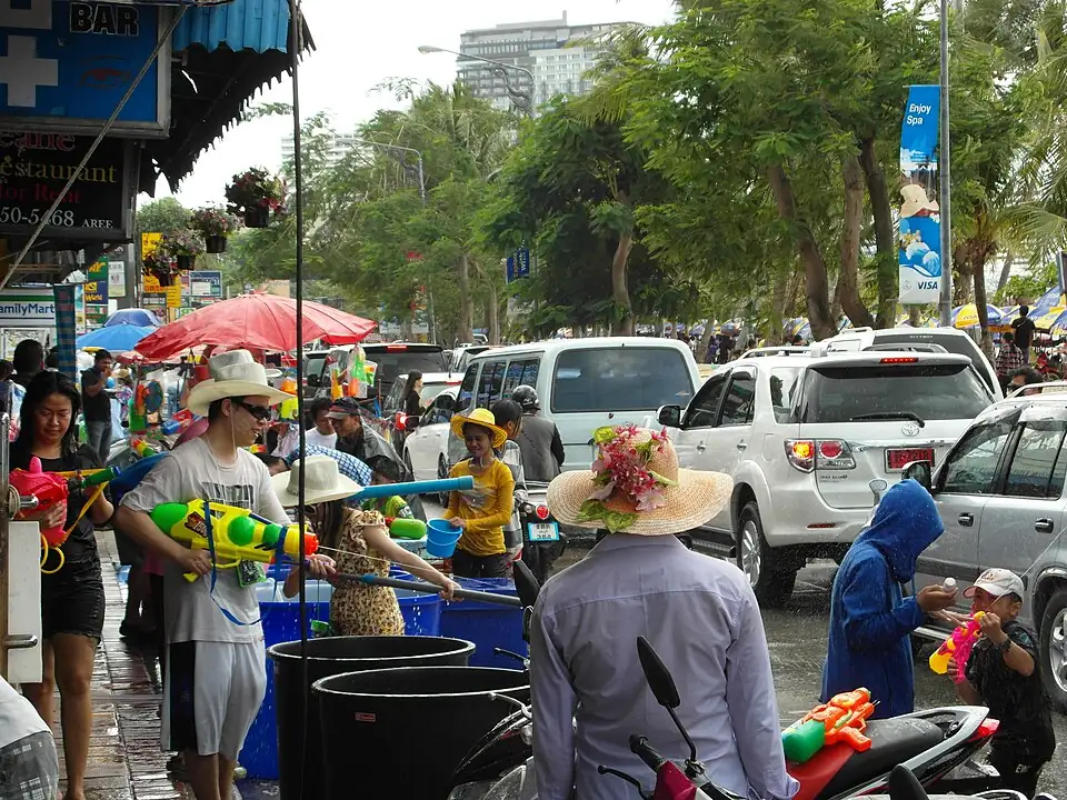 A crowded Pattaya street during the Thai New Year water festival, people with water guns beside barrels of water