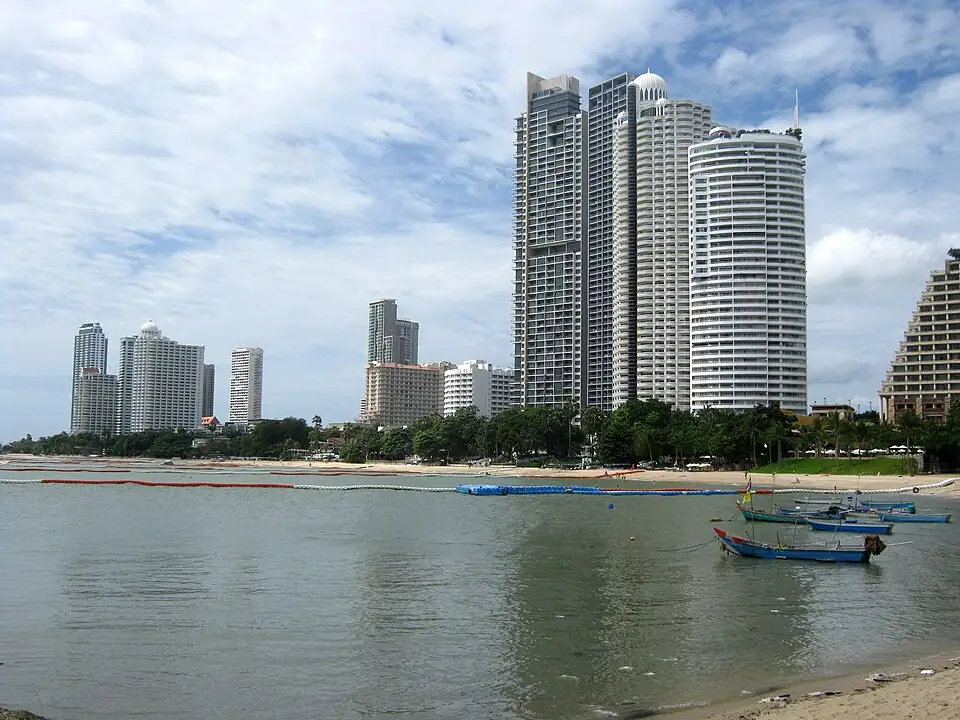 Wong Amat Beach at low tide, with long-tail boats in the shallows and high-rise towers behind the sand